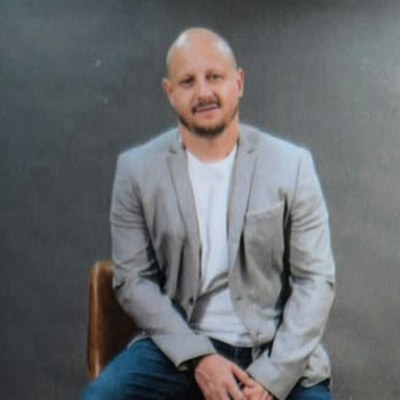Rafa Lima sentado em uma banqueta, de blazer cinza e camiseta branca